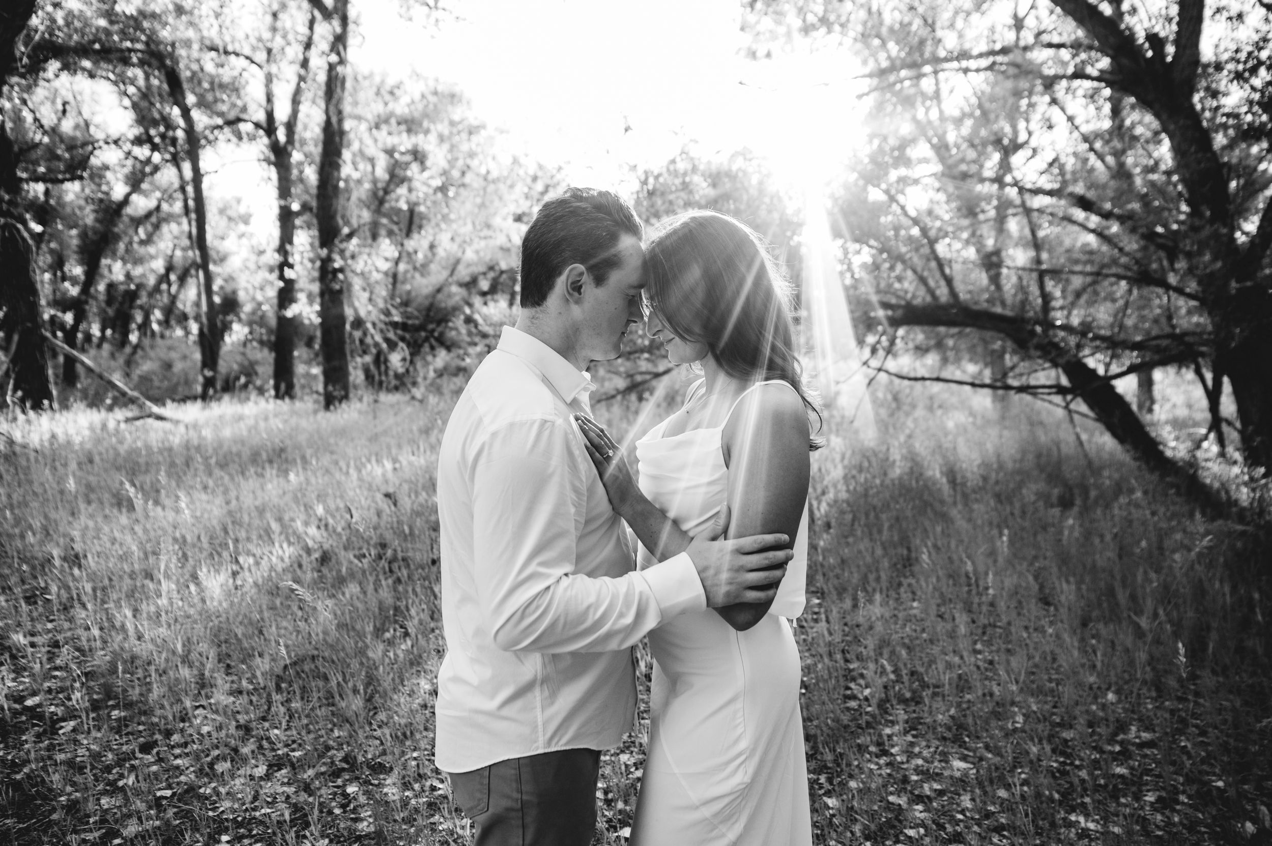 Black and white photo of a romantic couple embracing in a sunlit forest clearing, ideal for wedding photography inspiration.