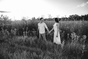 Black and white photo of a couple holding hands in a lush field at dusk.