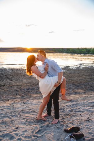 Couple sharing a romantic kiss on a sandy beach at golden sunset, barefoot with shoes left on the sand.