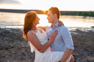 Couple embracing on a sandy beach at golden sunset, sharing a romantic moment by the water's edge.