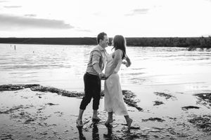 Couple dancing romantically on a beach shoreline at sunset in a black and white photo.