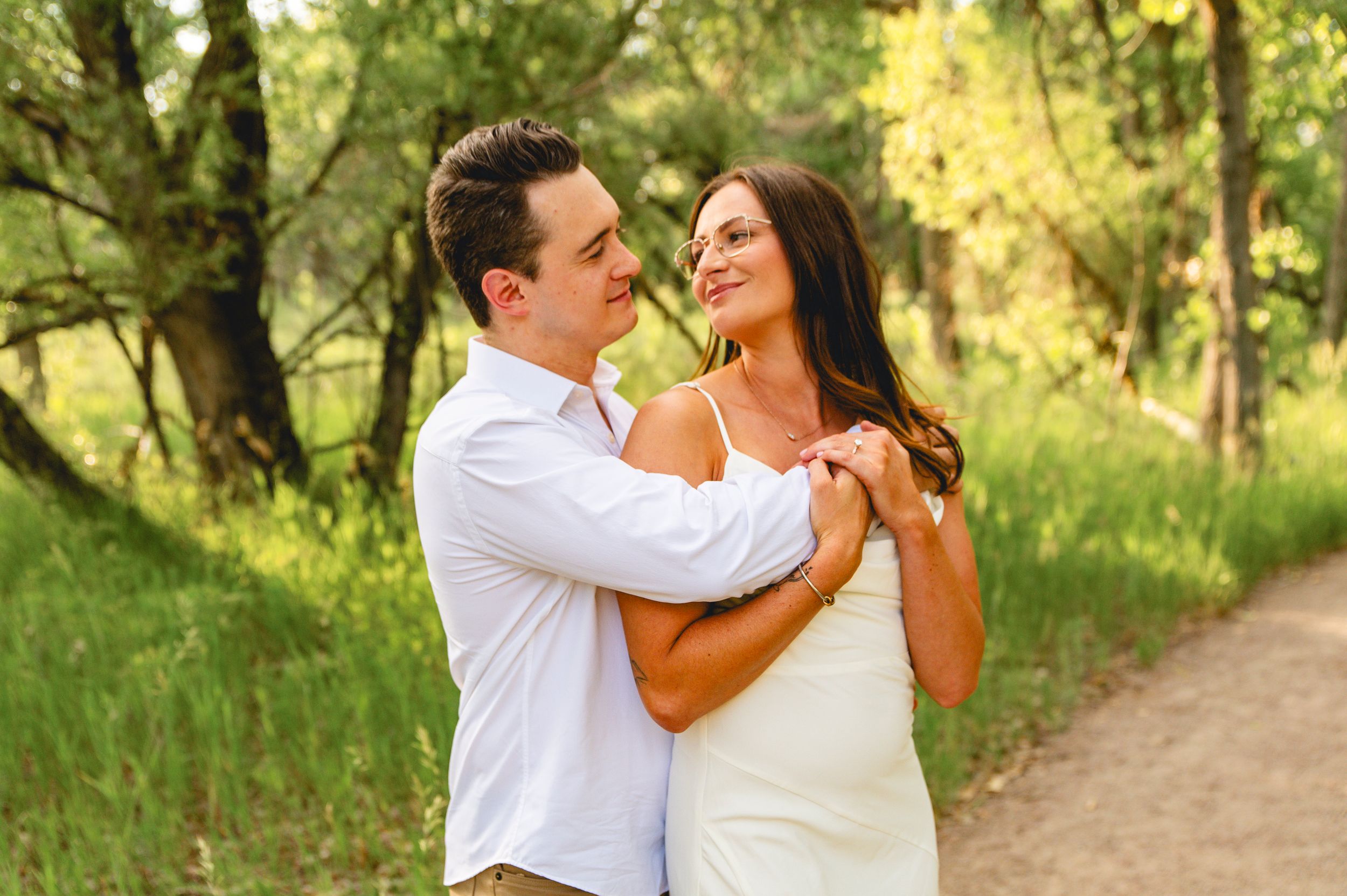 Romantic couple dancing on a woodland path surrounded by green trees in soft sunlight.
