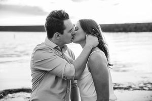 Black and white photo of a couple sharing a romantic kiss on a beach at sunset.