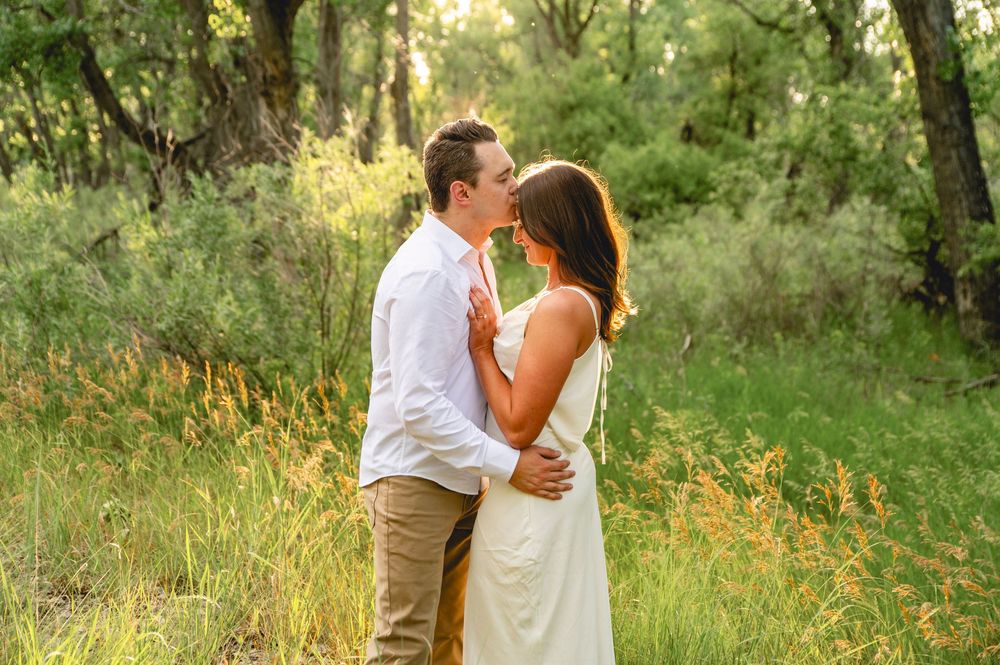 Couple embracing and kissing in a sunlit forest meadow, man in white shirt and woman in white dress.