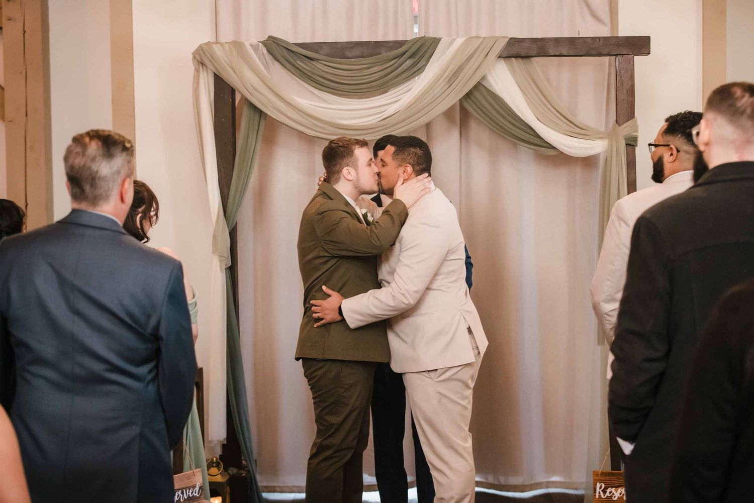 Couple sharing first kiss during indoor wedding ceremony at Briar Barn Inn with draped altar backdrop