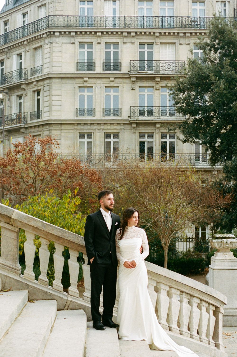 A bride and groom pose elegantly on stone steps in Paris. Parisian architecture, timeless paris film photography, paris 35mm wedding