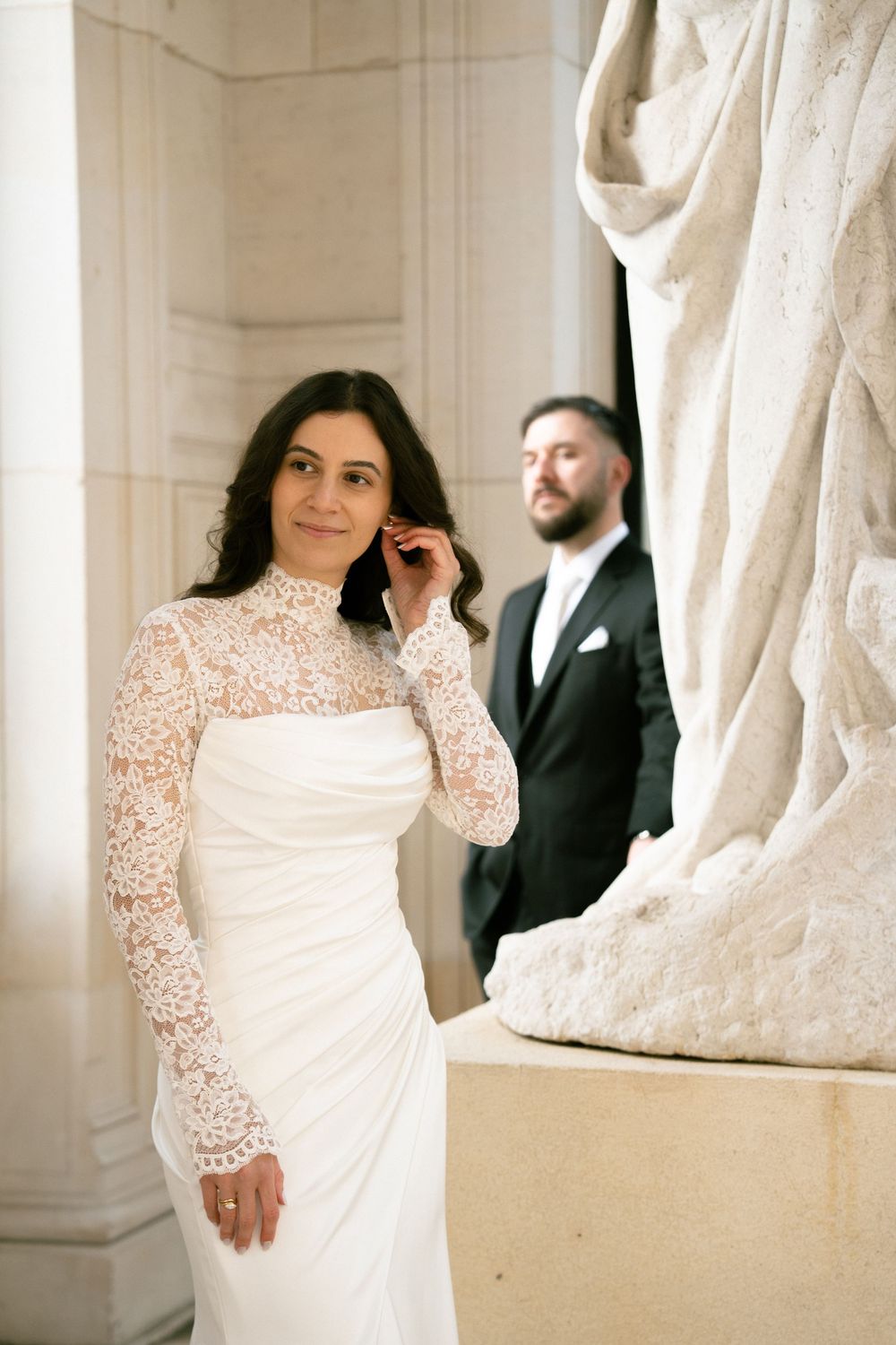 Bride in lace wedding gown poses near marble statue. Paris wedding photo location, paris wedding photographer, luxury paris wedding photo