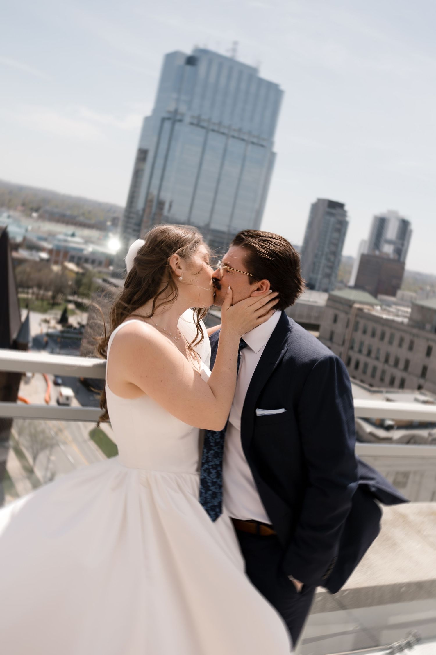 Bride and groom share a rooftop kiss with city skyline backdrop on their sunny spring wedding day.