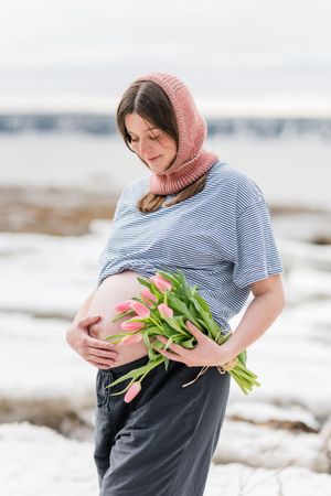 Portrait artistique d'une future maman sur les rives du fleuve en hiver qui tient à la main un bouquet de tulipes.