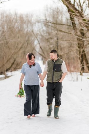 Futurs parents marchant main dans la main dans un sentier boisé au bord du fleuve st-laurent pour une séance fine art maternité