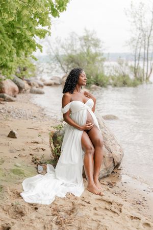 Future maman au bord de l’eau assise sur un rocher respirant l’air salin du fleuve