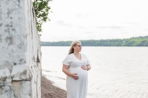 Future maman en robe blanche qui regarde au loin sur les rives du fleuve st-laurent