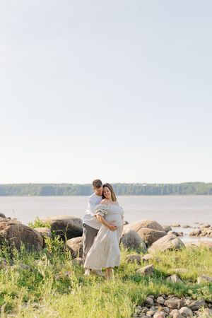 Portrait d'un couple attendant leur premier enfant sur les rives majestueuses du fleuve st-laurent dans des vêtements neutres