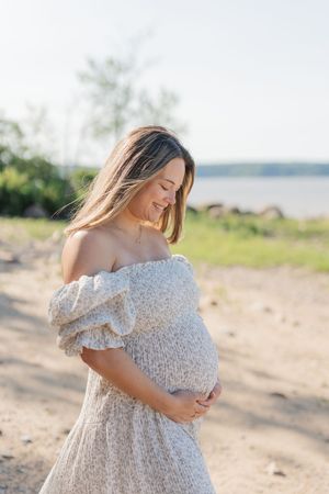 Future maman sur la plage qui regarde tendrement son ventre rond