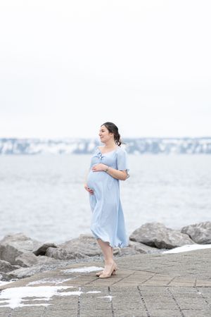 portrait fine art d'une future maman dans une robe bleue et légère au bord du fleuve St-Laurent un matin d'hiver