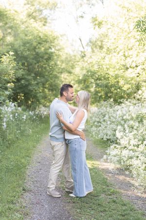 Couple de futurs parents dansant dans un sentier boisé bordé de fleurs blanches lors de leur séance au bord du fleuve à Saint-Augustin