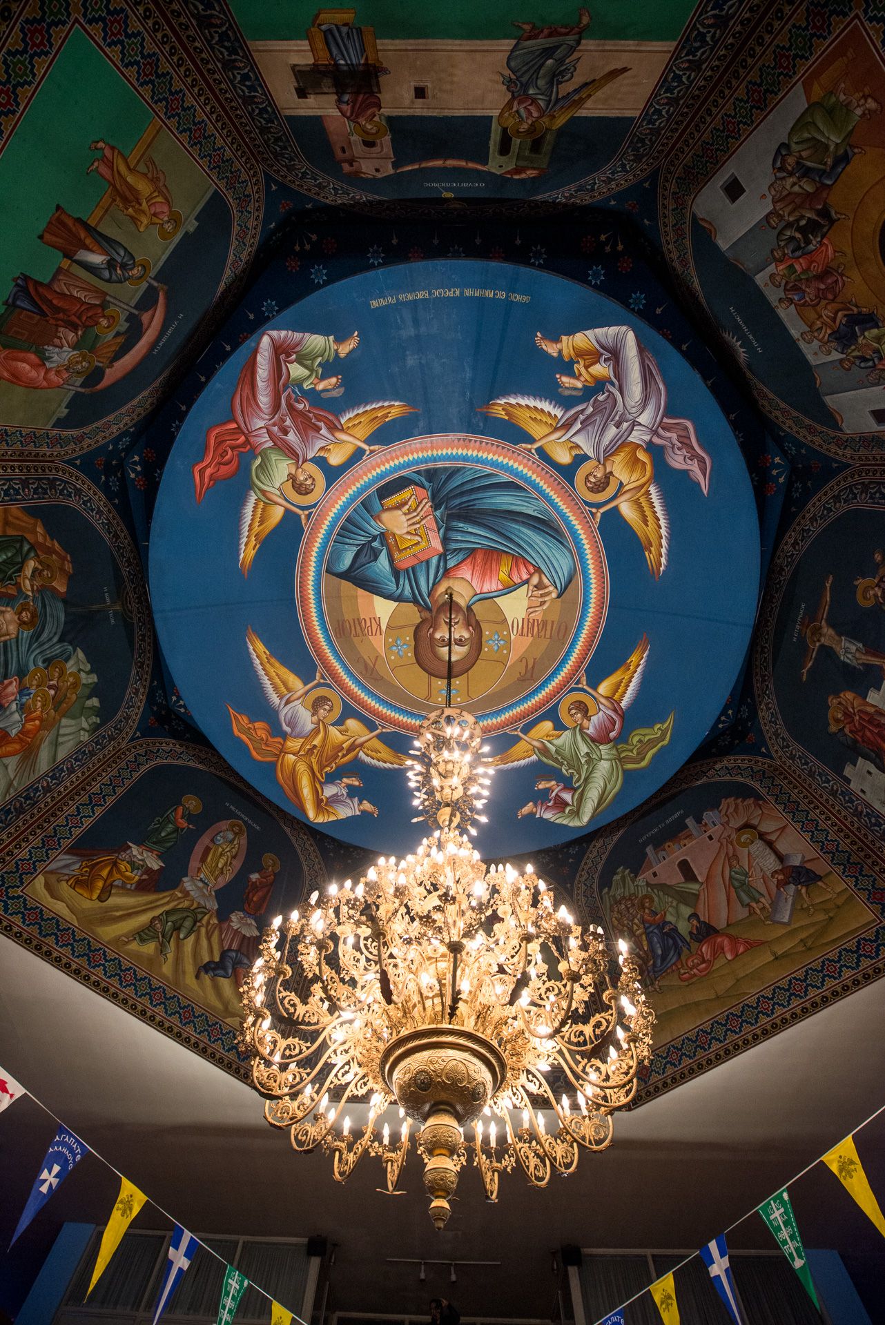Ornate Orthodox church ceiling with colorful religious fresco and gold chandelier below dome.