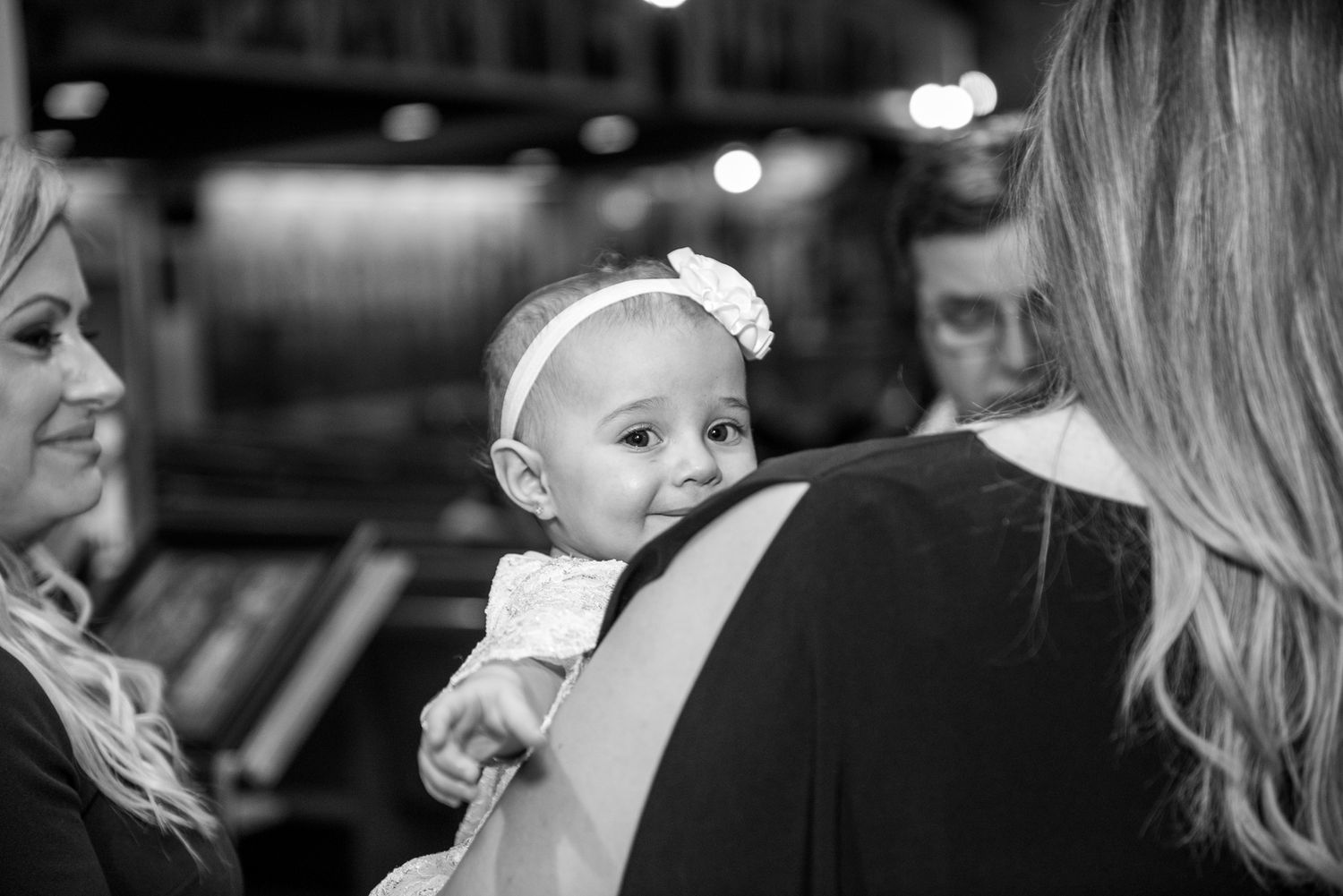 Baby girl with white bow headband being held at a Greek Orthodox christening ceremony.