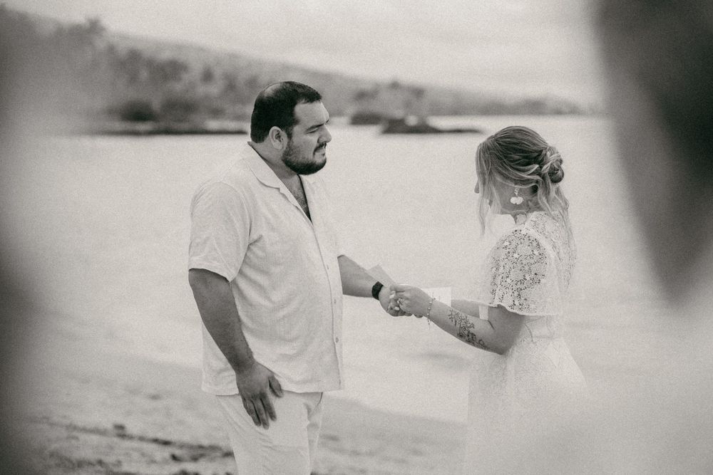 Black and white beach wedding photo of couple holding hands, bride in lace dress and groom in white shirt.