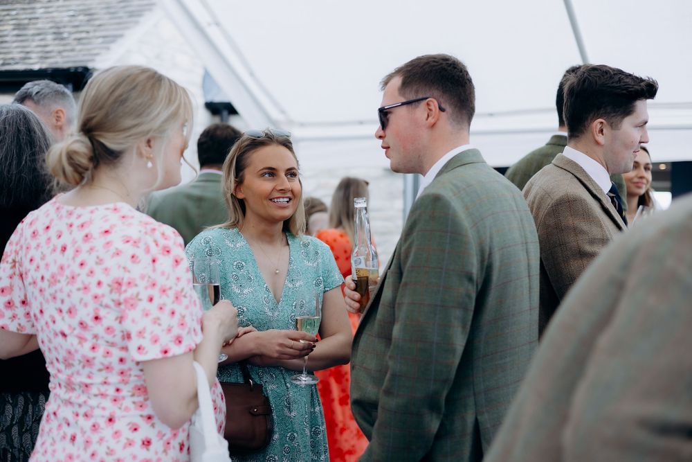 Guests in smart casual attire socializing outdoors at a christening reception under a marquee tent.