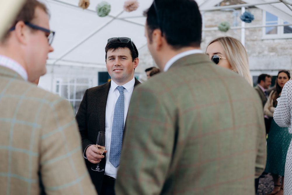Smartly dressed man in navy suit and blue tie socializing at an outdoor christening reception.