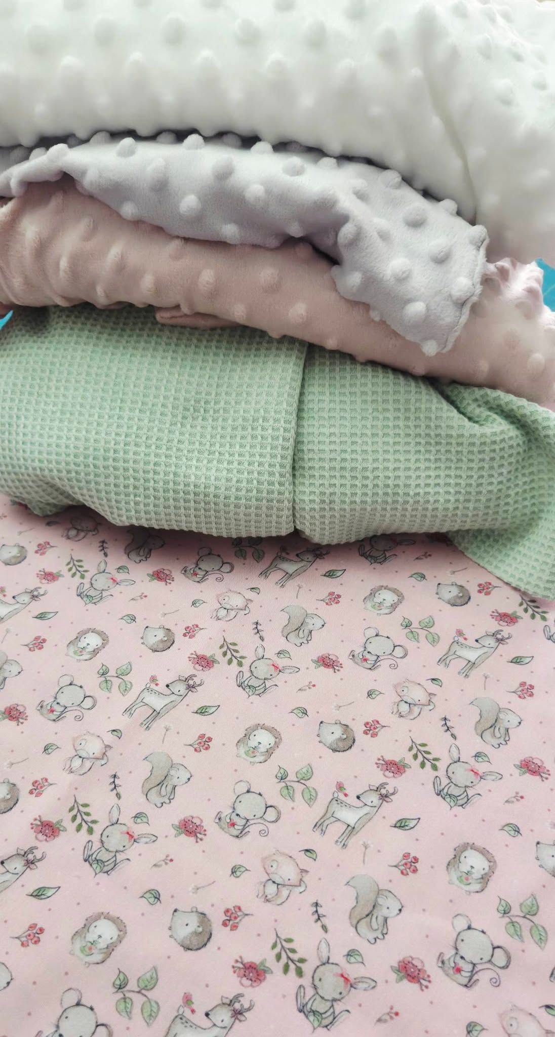 Stack of soft baby blankets including pink minky dot, green waffle knit, and woodland animals print fabric.