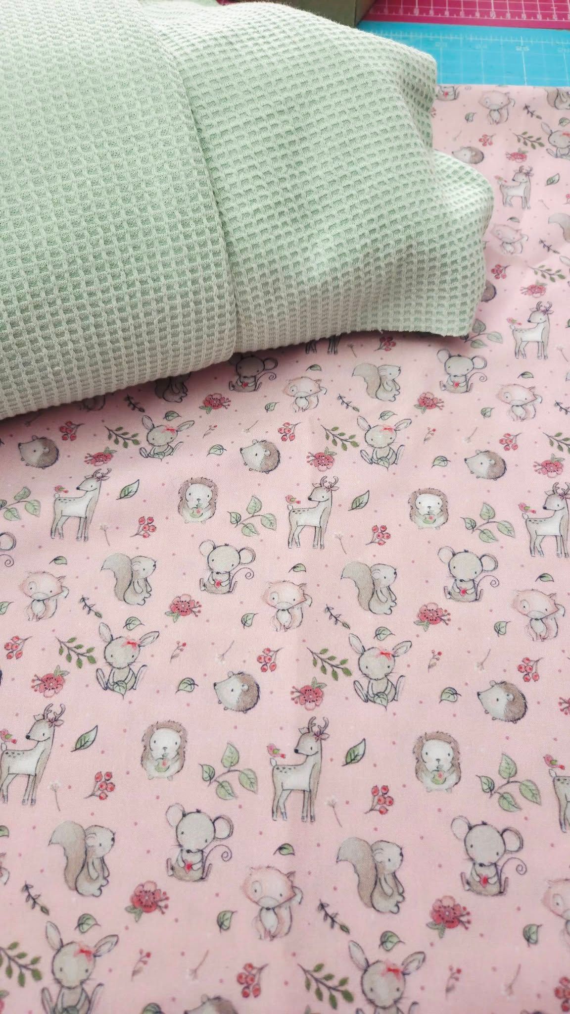 Pink baby fabric featuring cute woodland animals displayed with a mint green waffle knit pillow.
