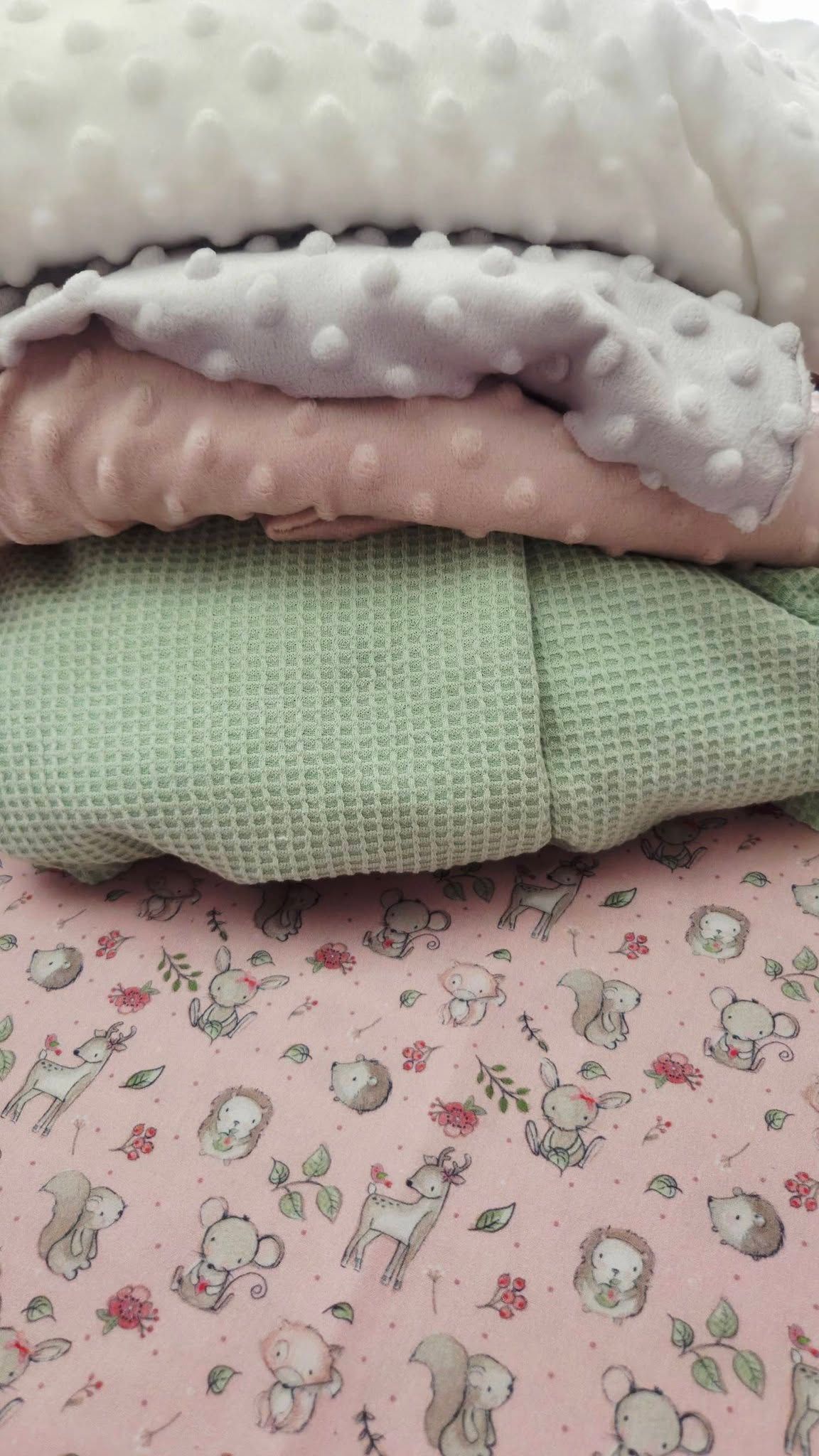 Stack of folded baby blankets in pink minky dot, sage green waffle knit, and pink woodland animals cotton fabric.