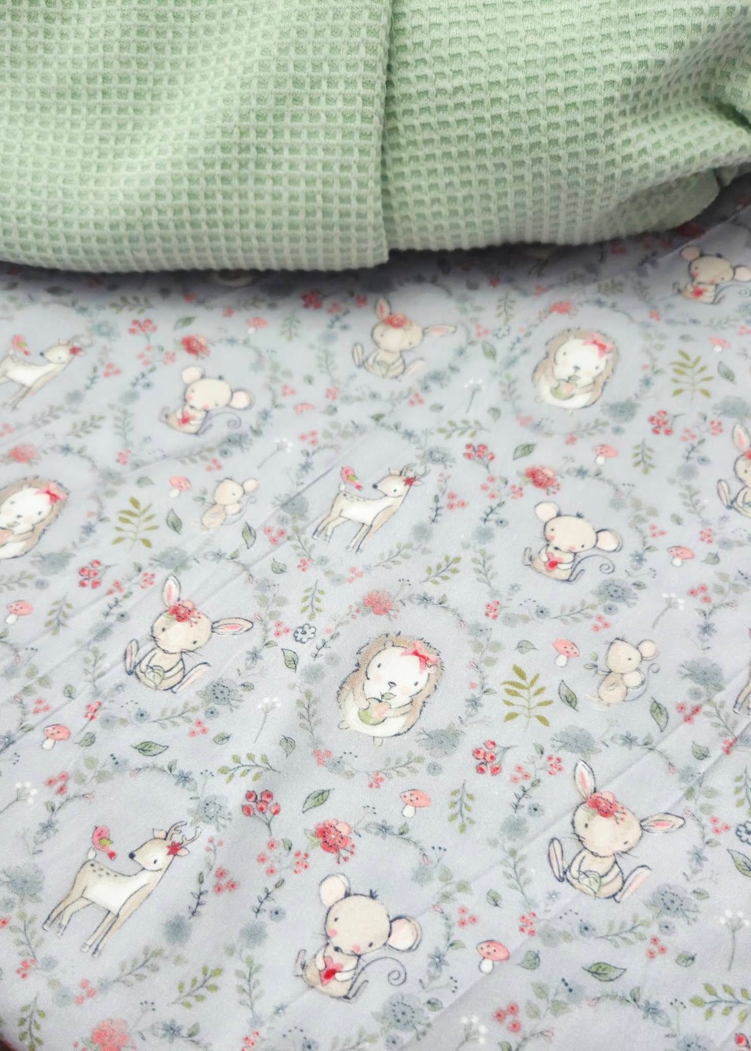 Light blue baby fabric featuring woodland animals, bunnies, deer, and floral wreaths, paired with a green waffle knit blanket.