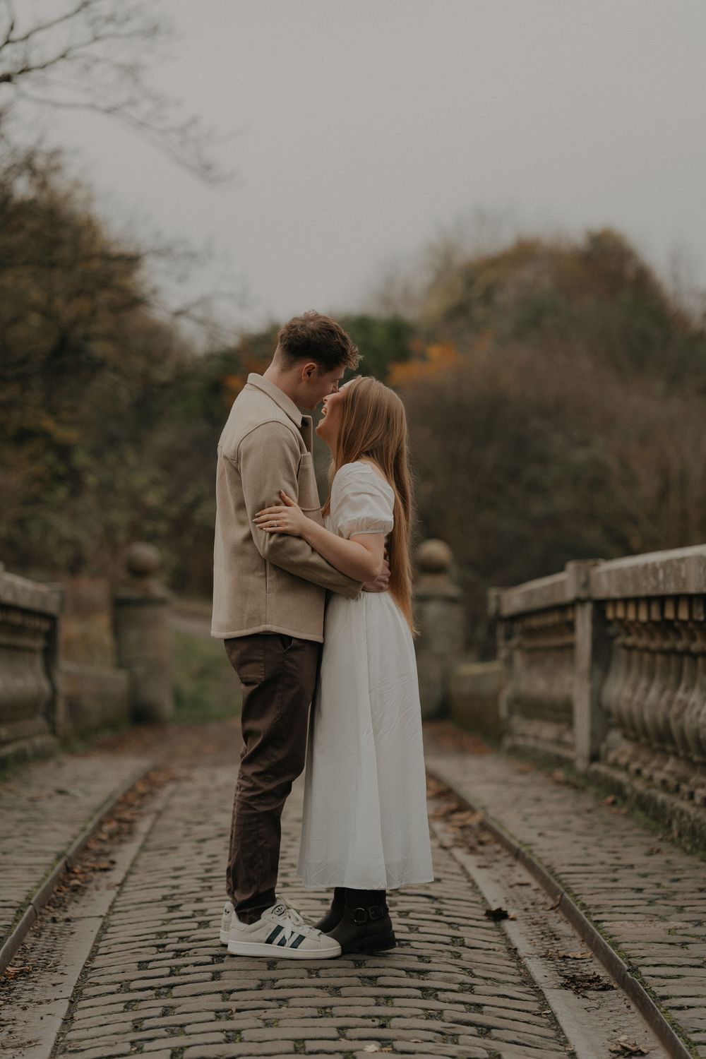 Couple embracing tenderly on a cobblestone bridge surrounded by autumn foliage.