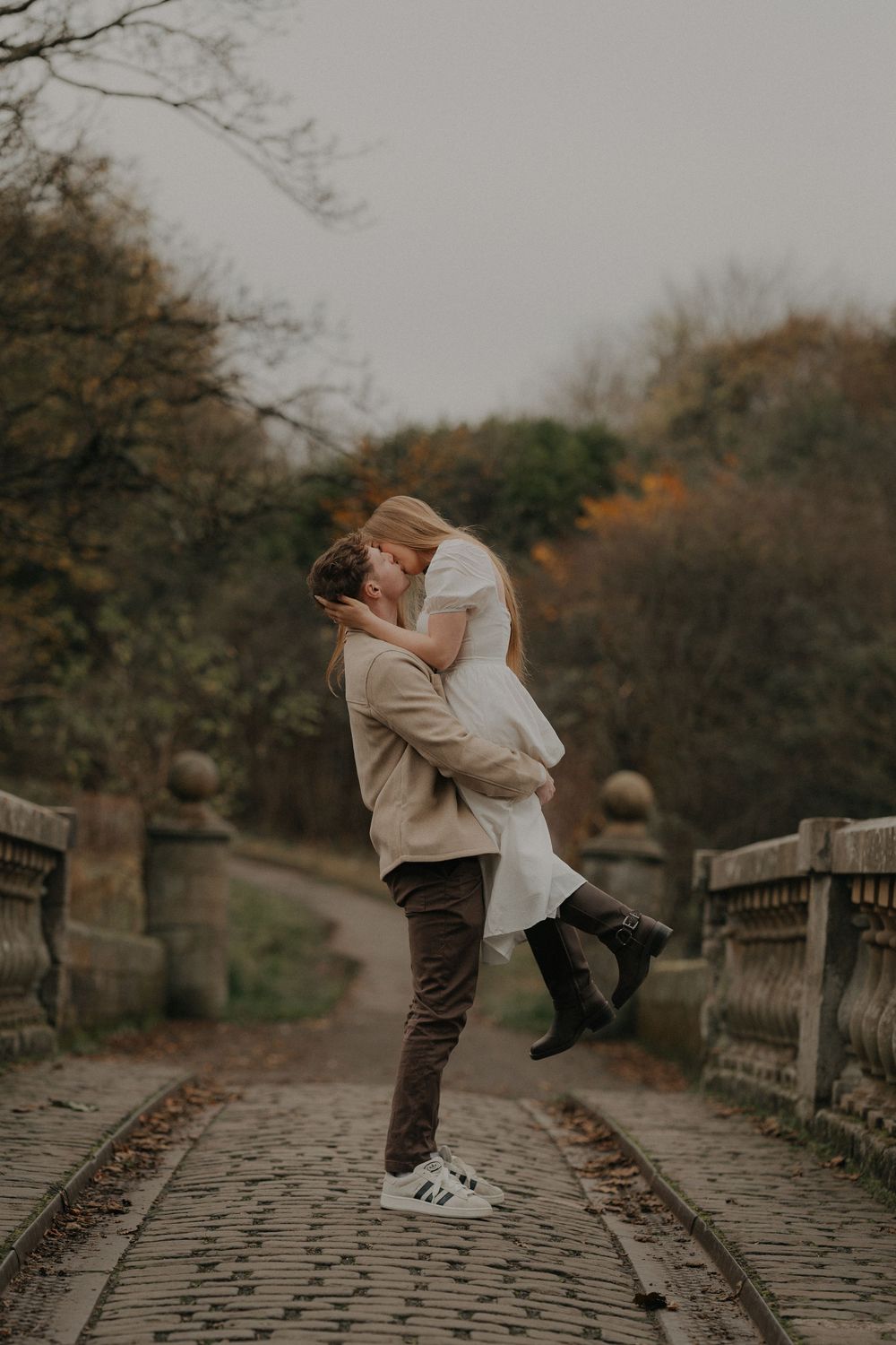 Man lifting woman for a romantic kiss on a scenic cobblestone bridge in fall.