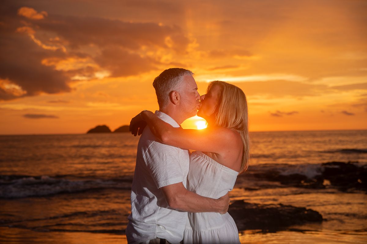 Couple sharing a romantic kiss on the beach during a stunning golden sunset over the ocean.