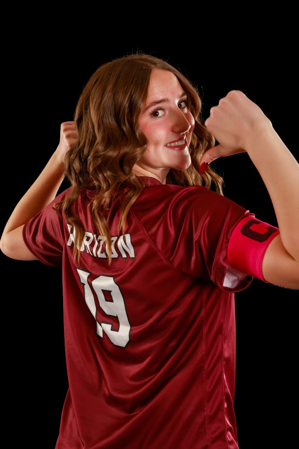 Soccer player in maroon jersey number 19 poses in dynamic action pose against dark backdrop.