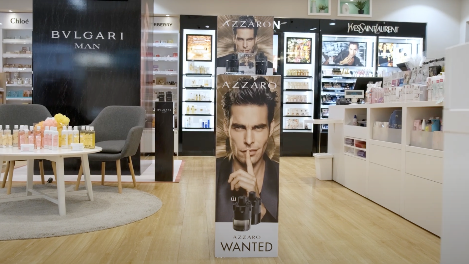Luxury retail display inside a store showing perfume advertisements and product displays on white shelving units.
