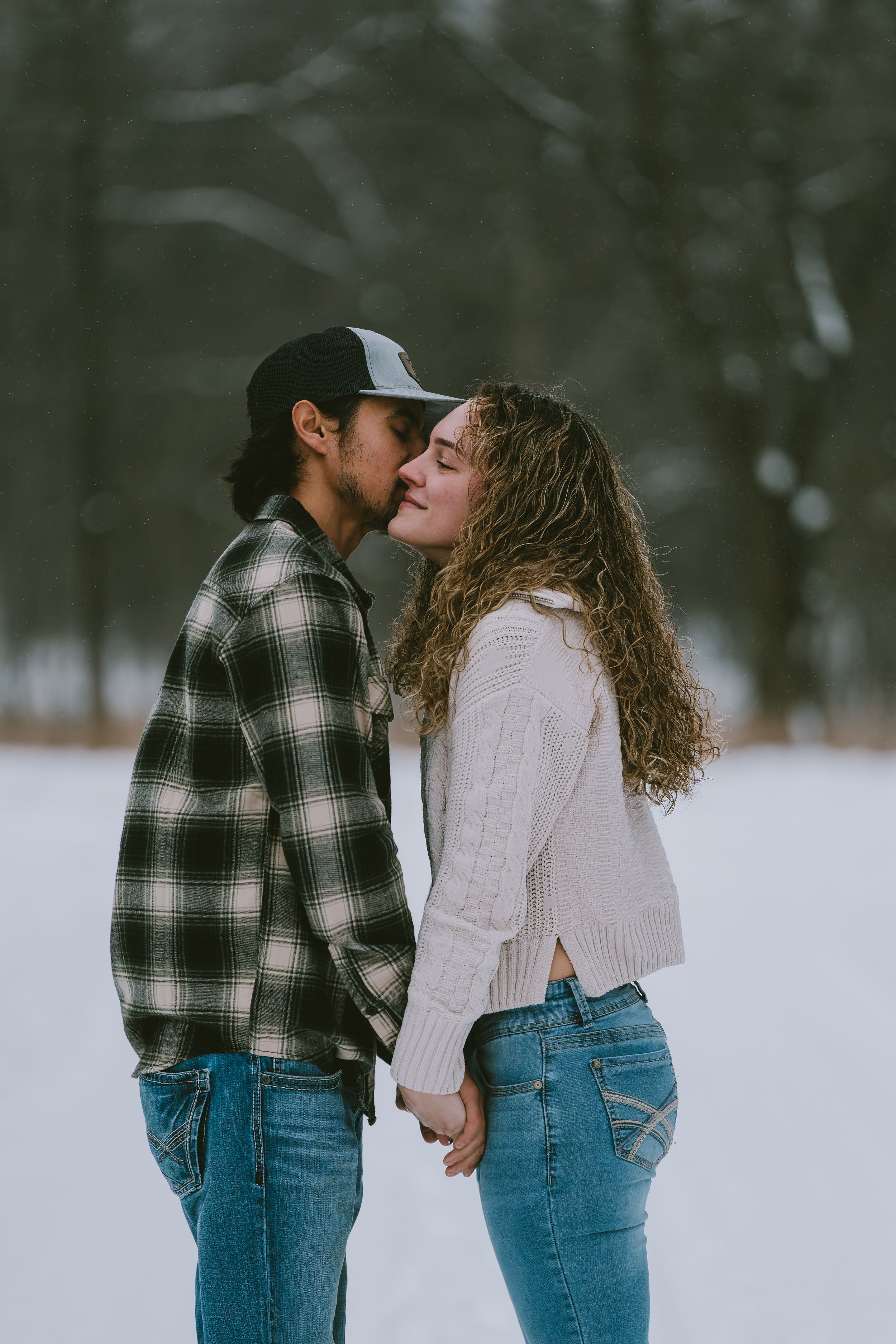 Romantic couple in winter attire holding hands and sharing an intimate moment in a snowy outdoor setting.