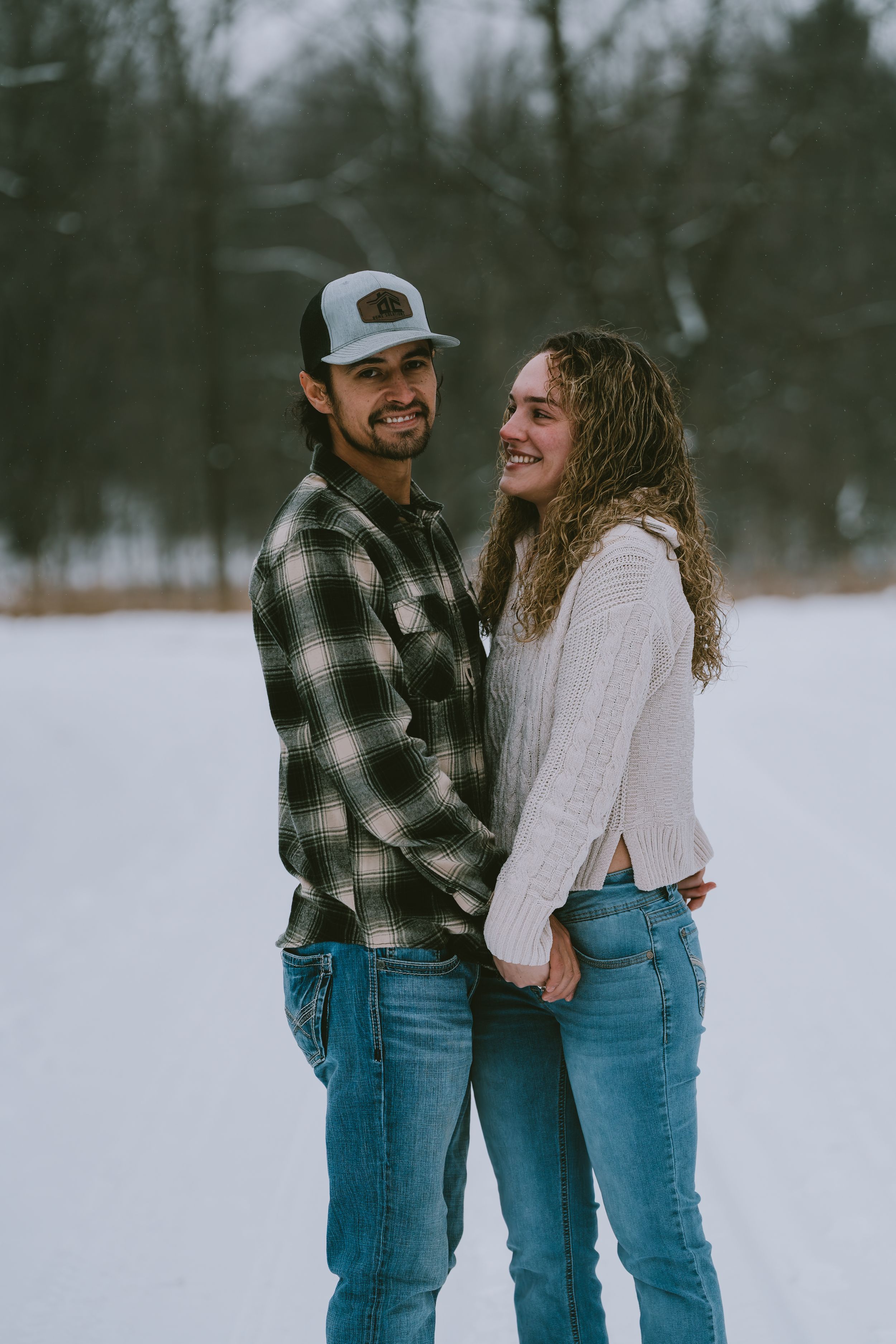 Couple in casual winter outfits sharing an intimate moment while standing in snowy landscape.
