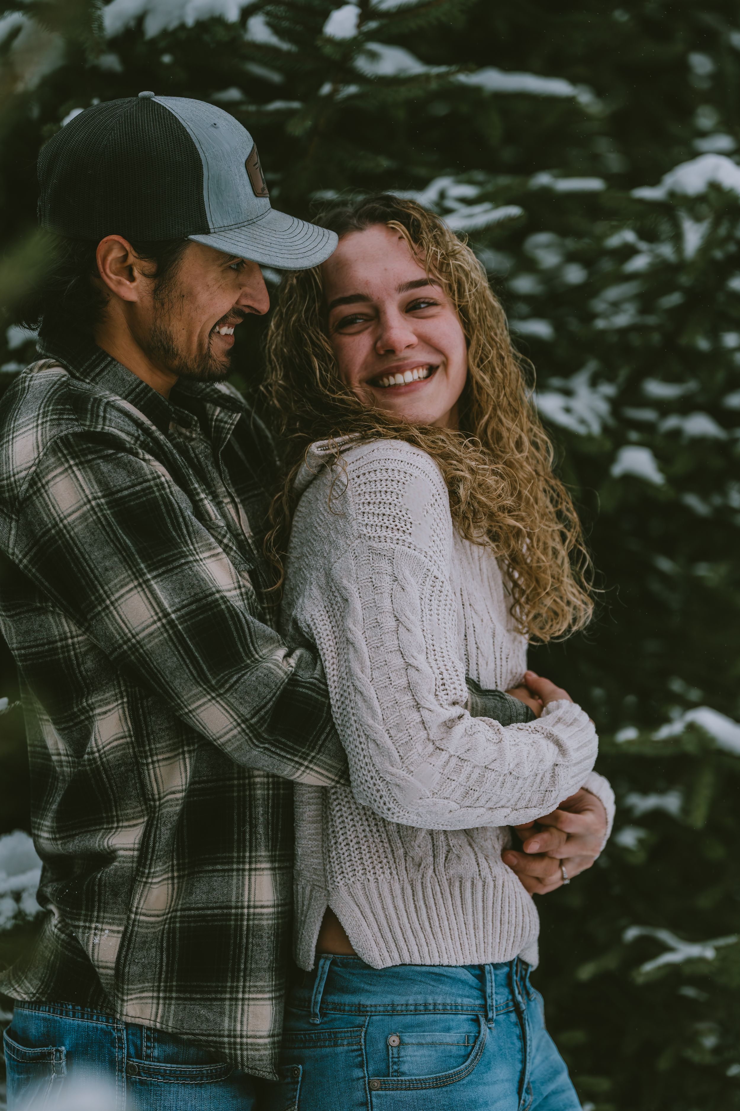 A couple embraces and laughs together while wearing casual winter clothing against a dark background.