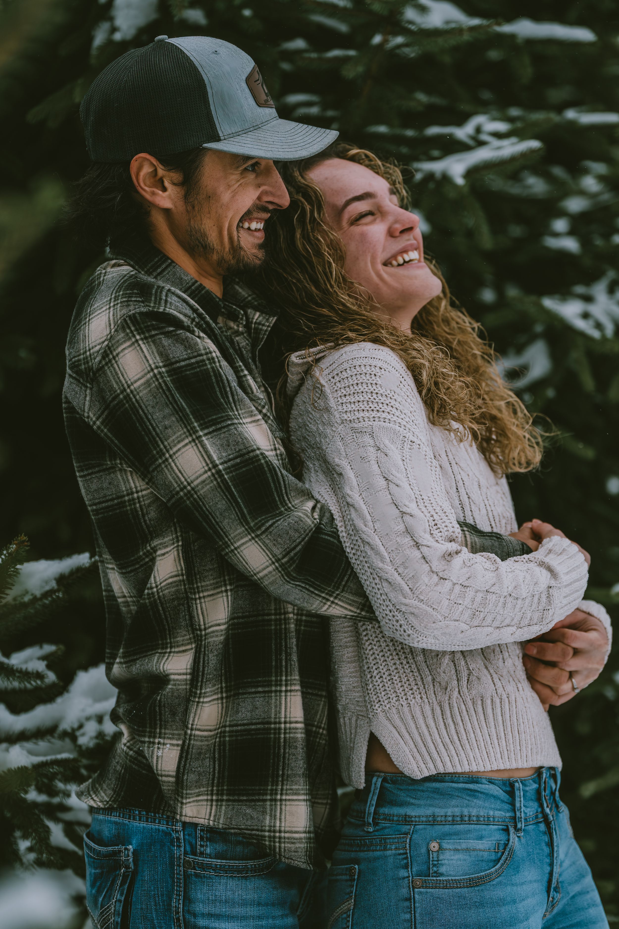 Couple embracing and laughing together outdoors in winter, wearing casual plaid shirt and white sweater.