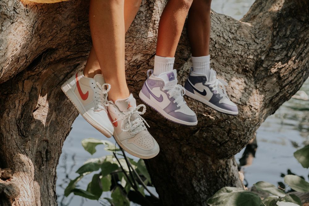 Close-up shots of feet wearing trendy white sneakers standing on a tree branch in an outdoor setting.