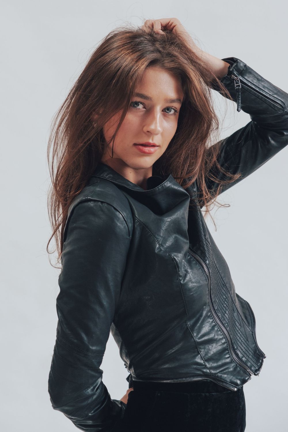 A model poses in a black leather jacket with flowing brown hair against a white background.