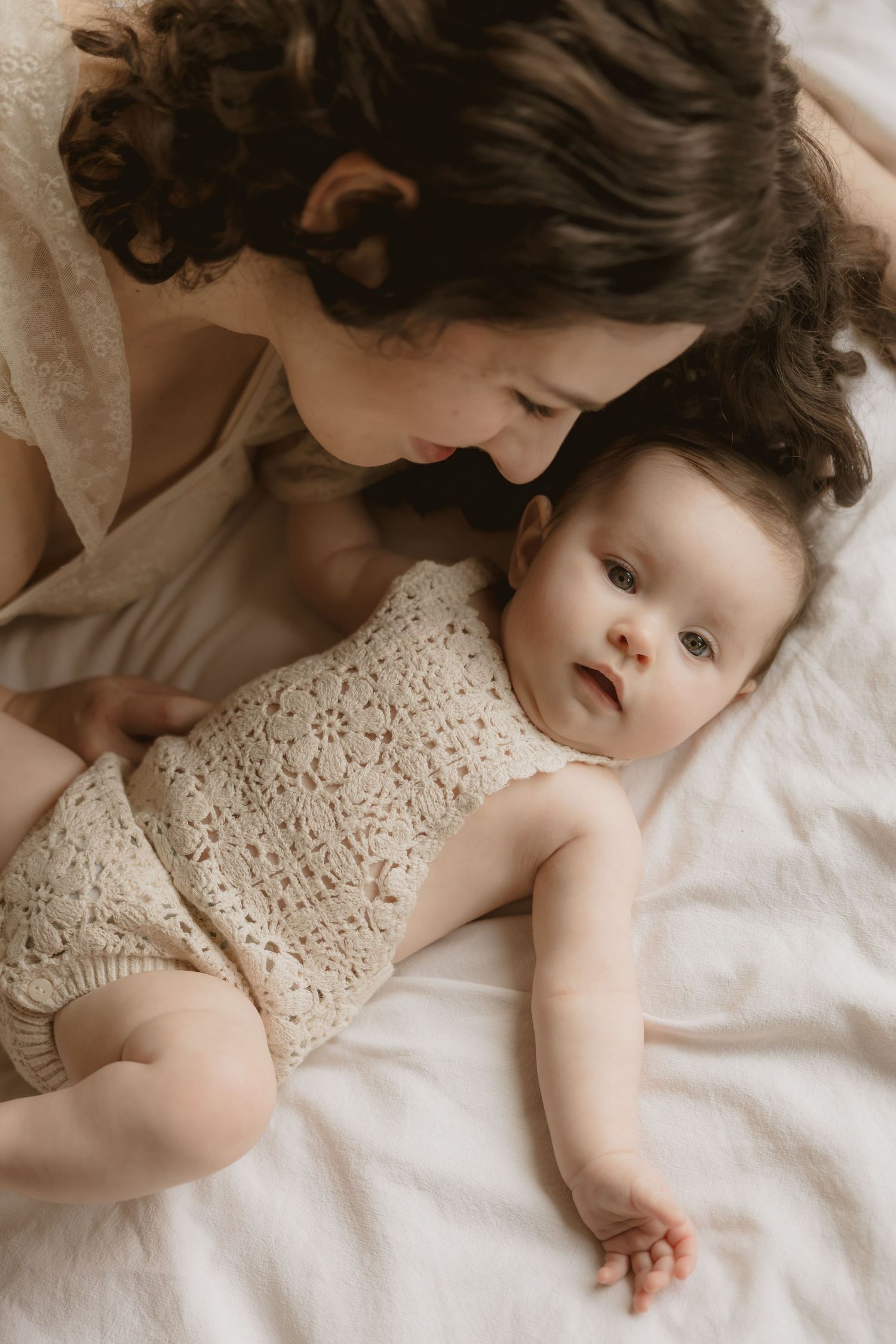 A joyful moment captured in a field of tall grass as a mother wearing white embraces her baby in sweet affection.