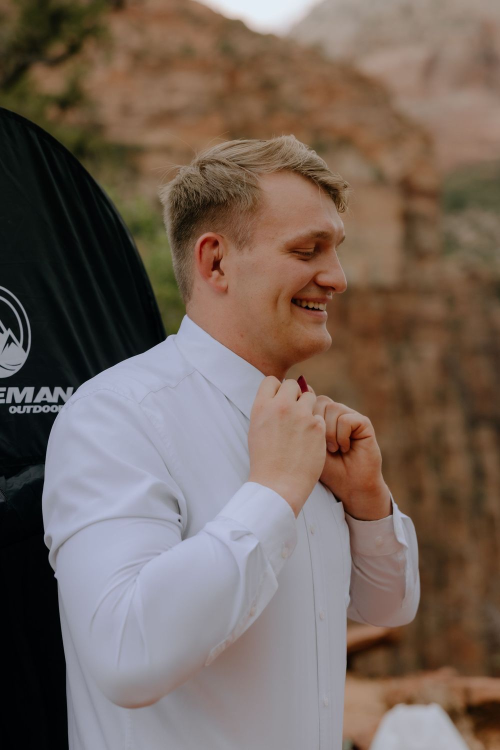 A person in a white dress shirt shows a range of emotional expressions while adjusting their collar against a natural backdrop.