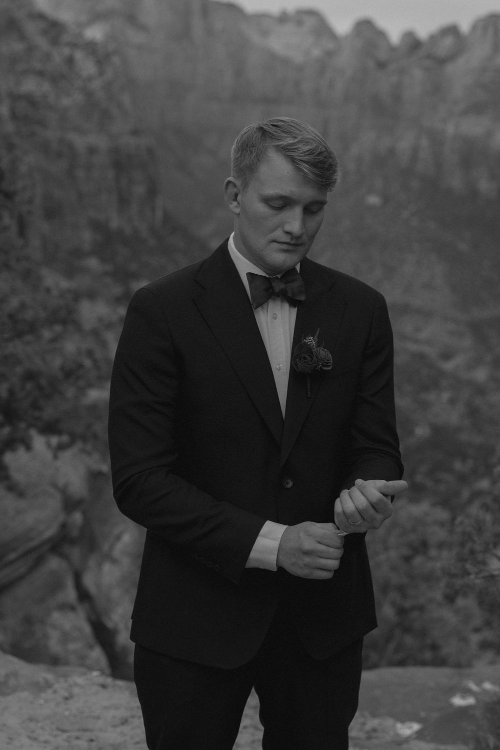 Black and white photo of a wedding couple standing on rocky terrain with towering canyon walls behind them.