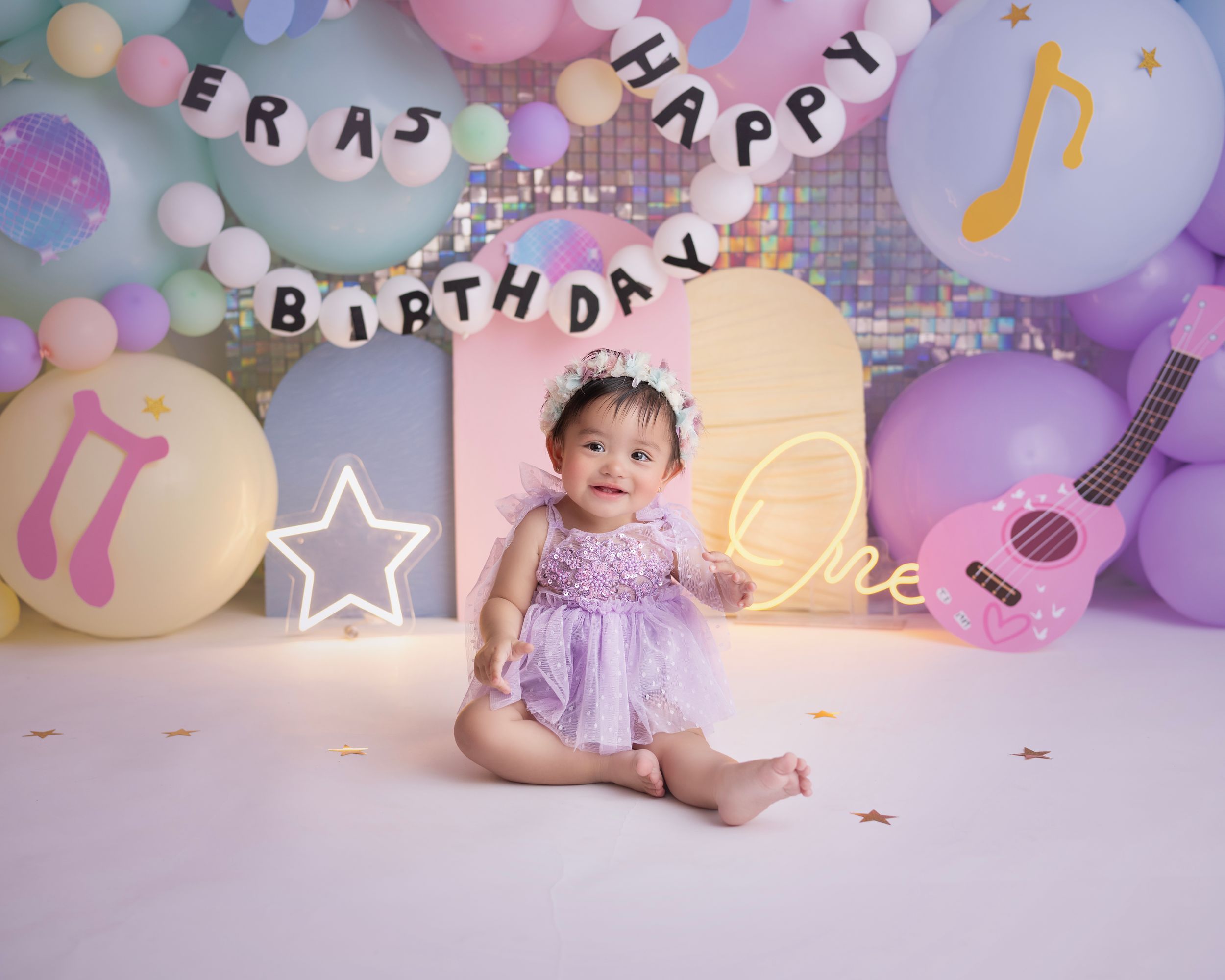 Music-themed first birthday celebration setup with pastel balloon arch, musical note decorations, and guitar props in soft purple tones.