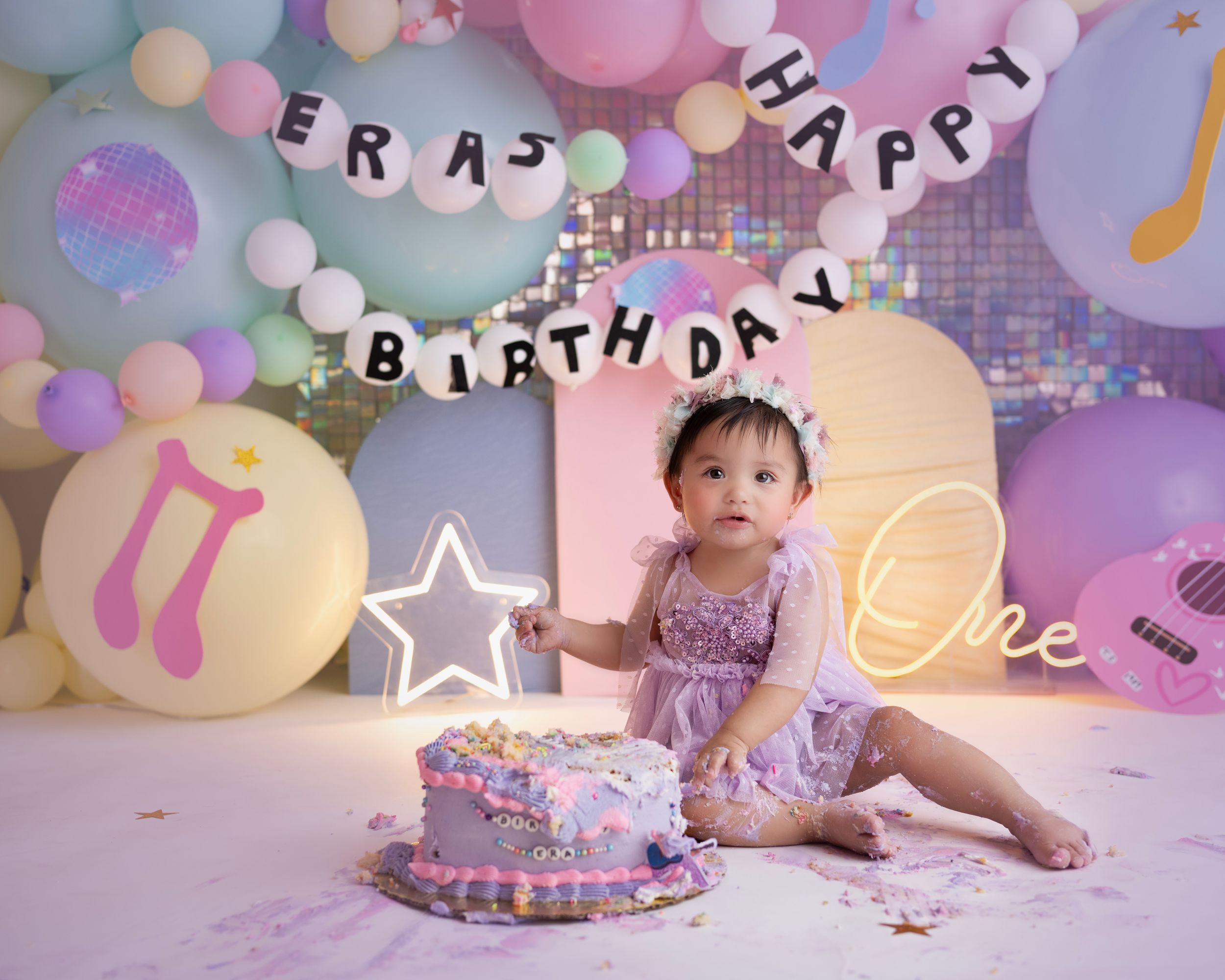 Festive cake smash photography setup with musical themed decorations and pastel colored balloons.