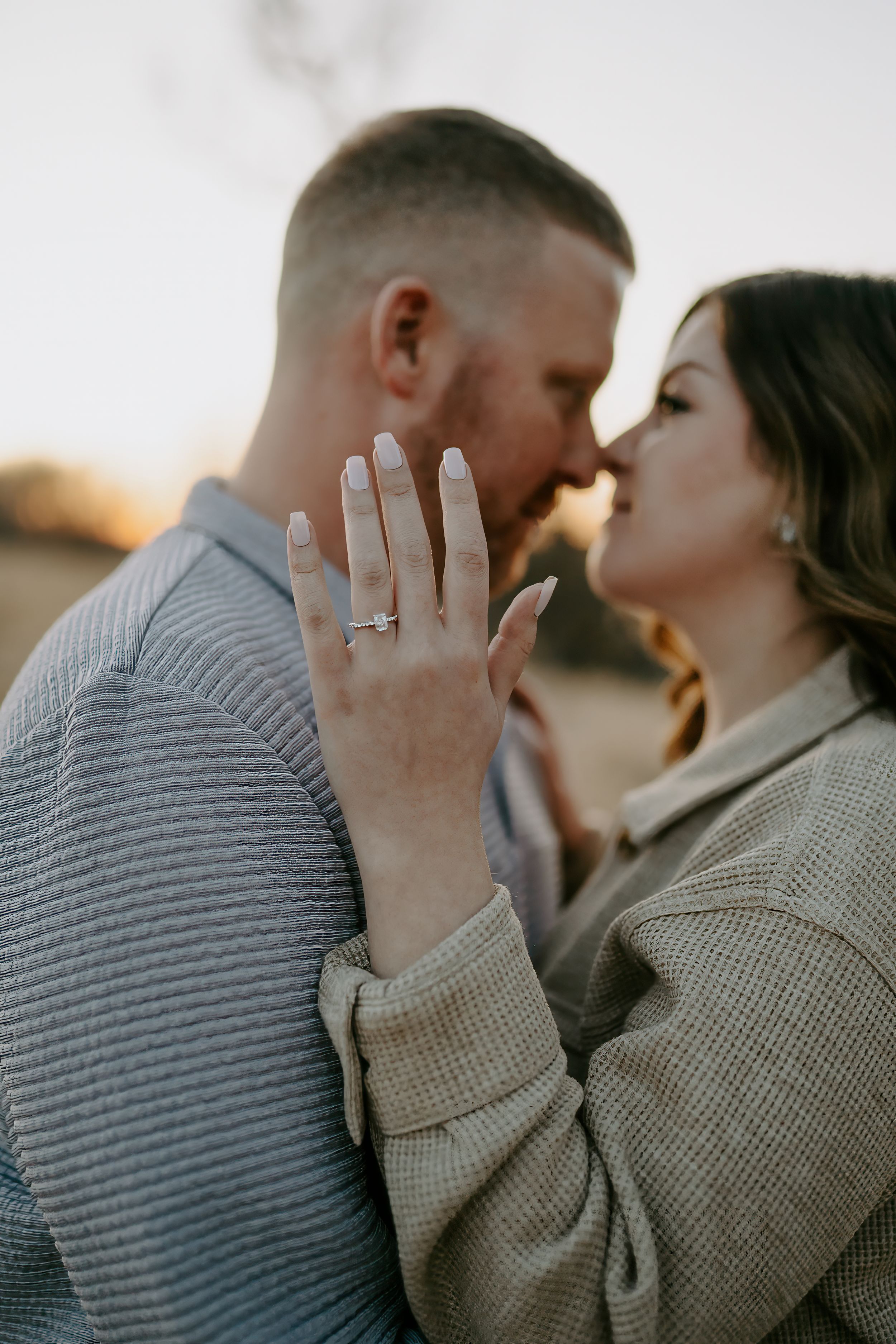 Close-up engagement photos showing hands with rings during an intimate moment at sunset.