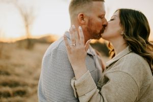A tender moment between a couple wearing cozy sweaters during a golden sunset photoshoot.