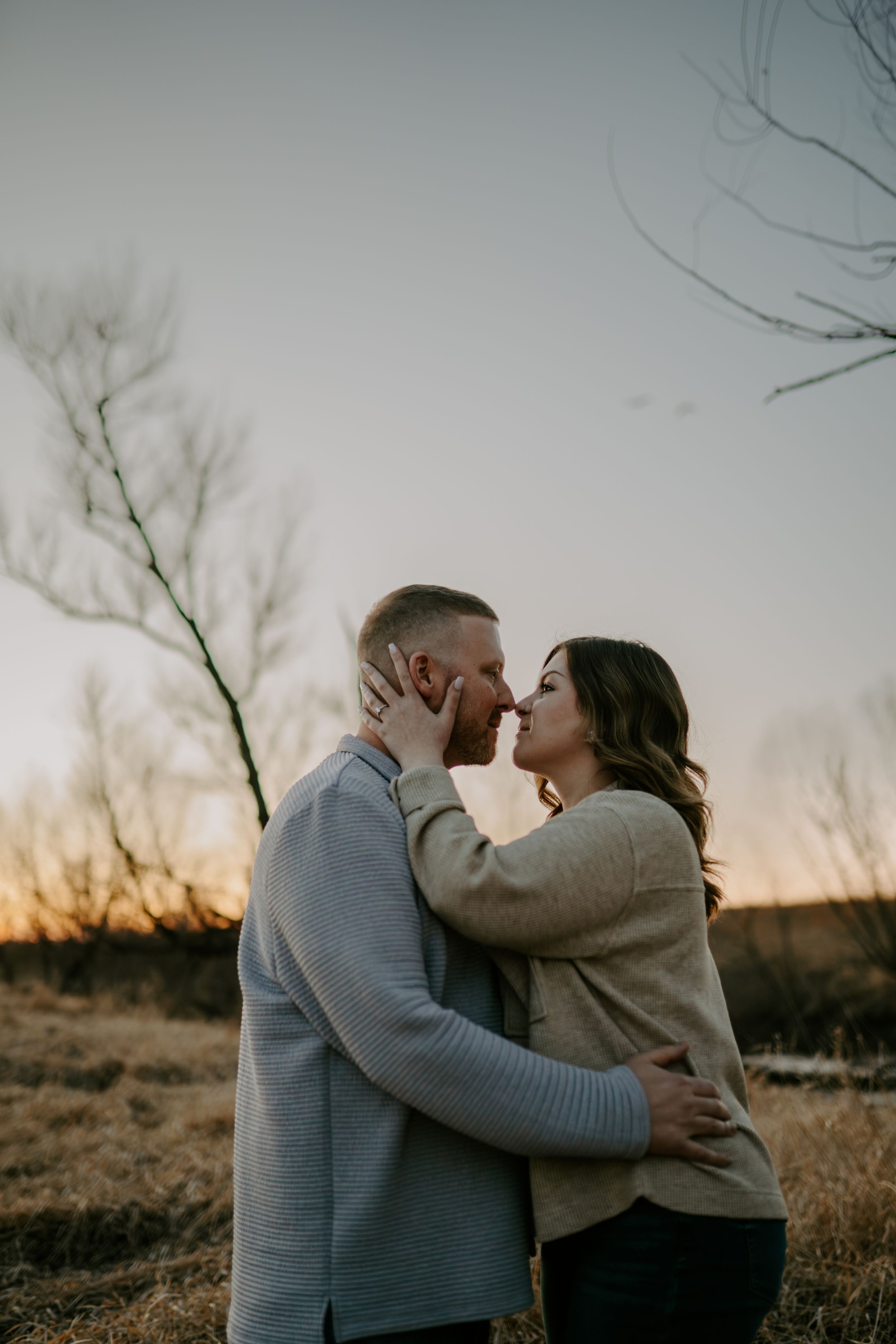 A romantic sunset photoshoot showing a couple embracing in warm winter sweaters.