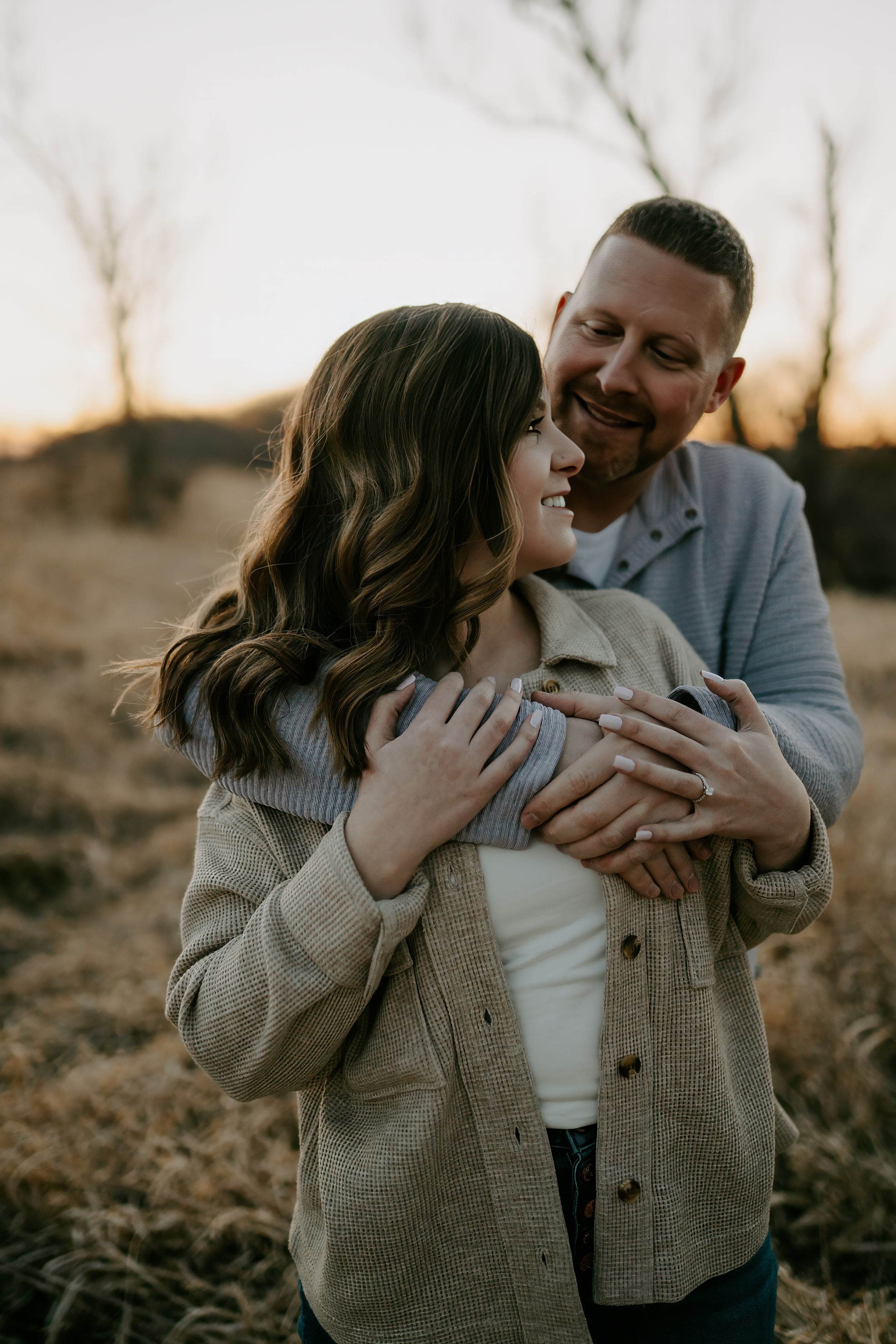 A romantic couple shares a tender embrace at sunset in a rustic outdoor setting.