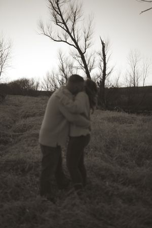 A black and white photo captures an intimate moment between a couple in a field at dusk.